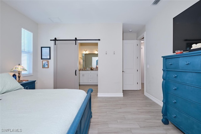 bedroom with a barn door, visible vents, baseboards, connected bathroom, and light wood-style flooring