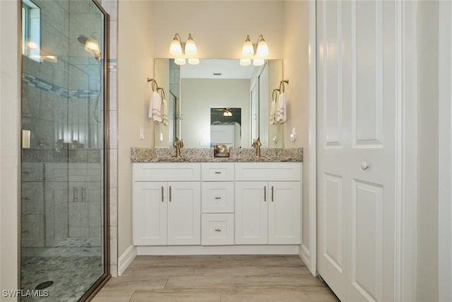 bathroom featuring double vanity, wood finish floors, a stall shower, and a sink