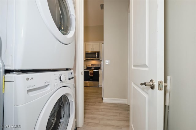 clothes washing area with stacked washer and dryer, wood tiled floor, laundry area, and baseboards