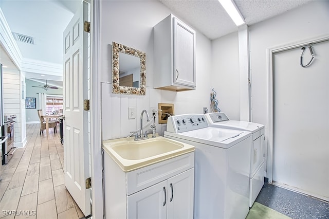 washroom featuring visible vents, cabinet space, washing machine and dryer, a sink, and a textured ceiling