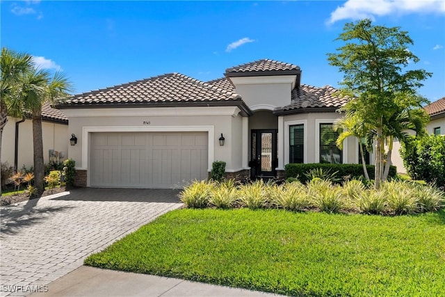 mediterranean / spanish home with a tile roof, a front yard, stucco siding, decorative driveway, and a garage