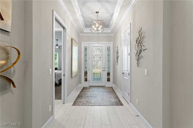 foyer entrance featuring an inviting chandelier, a raised ceiling, ornamental molding, and baseboards