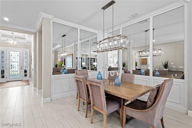 dining space with crown molding, a decorative wall, a notable chandelier, and visible vents