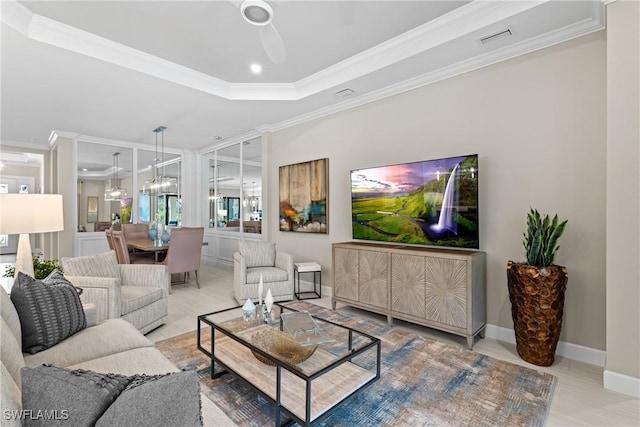 living room with a ceiling fan, baseboards, visible vents, a tray ceiling, and ornamental molding