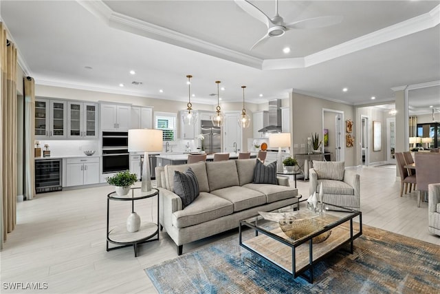 living room featuring beverage cooler, a ceiling fan, a tray ceiling, recessed lighting, and light wood-style floors