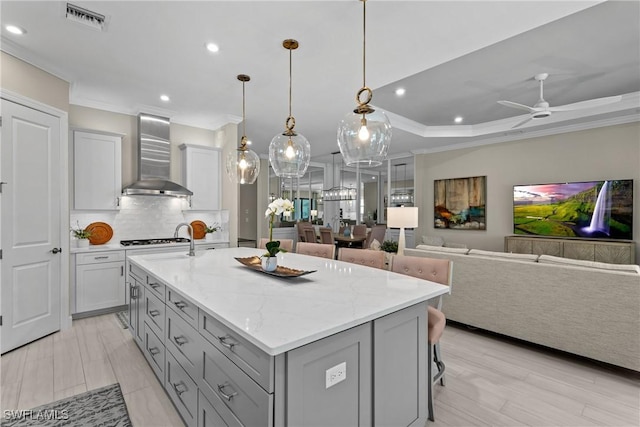kitchen with wall chimney range hood, gray cabinetry, recessed lighting, and ornamental molding