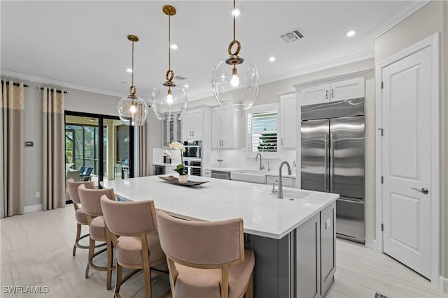 kitchen featuring visible vents, a kitchen island with sink, ornamental molding, a sink, and appliances with stainless steel finishes