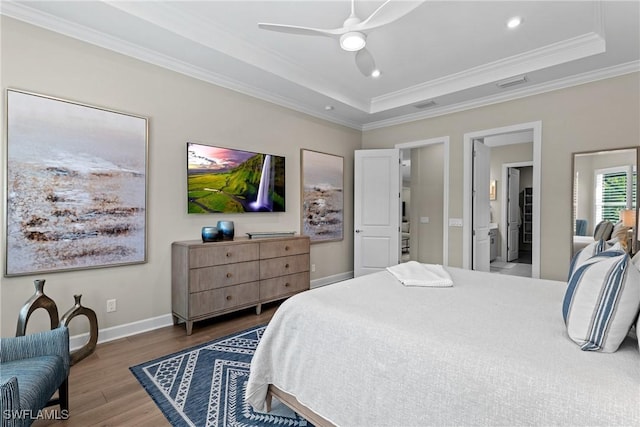 bedroom with a tray ceiling, wood finished floors, baseboards, and ornamental molding