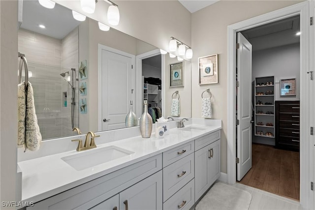full bathroom featuring double vanity, a walk in closet, a tile shower, and a sink