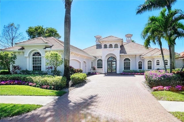 mediterranean / spanish house featuring an attached garage, stucco siding, decorative driveway, and french doors