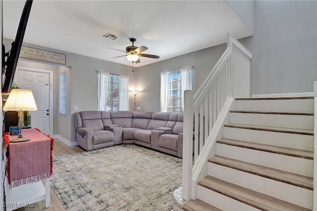 living room featuring light wood finished floors, visible vents, ceiling fan, baseboards, and stairs