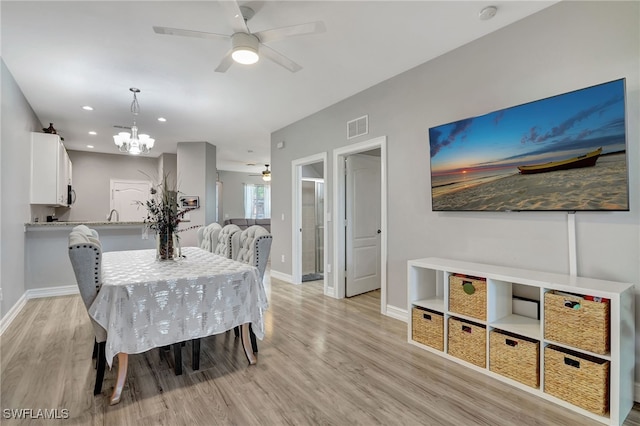 dining room with baseboards, ceiling fan with notable chandelier, visible vents, and light wood-style floors