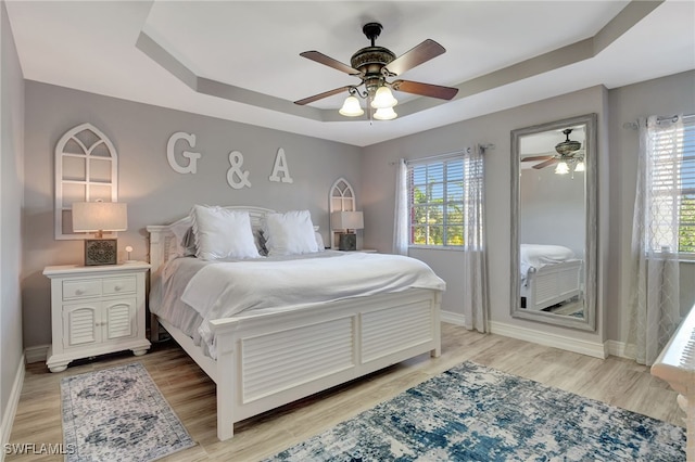 bedroom featuring a tray ceiling, multiple windows, baseboards, and wood finished floors