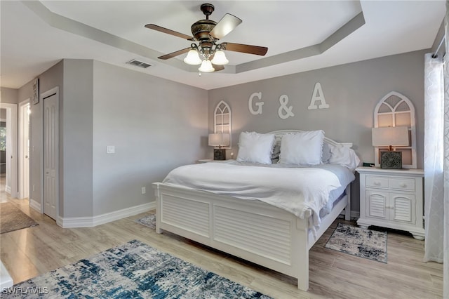 bedroom featuring visible vents, a raised ceiling, a ceiling fan, baseboards, and light wood-style flooring