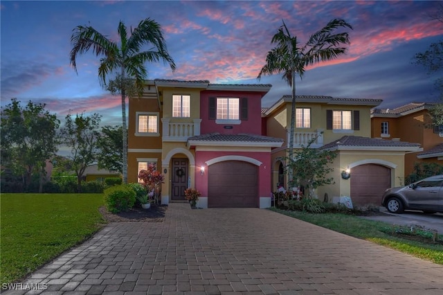 mediterranean / spanish-style house with decorative driveway, a balcony, a lawn, and stucco siding