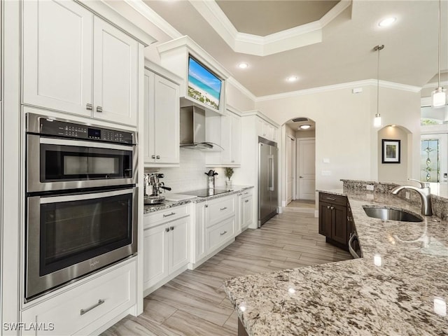 kitchen featuring arched walkways, decorative backsplash, appliances with stainless steel finishes, a sink, and wall chimney exhaust hood