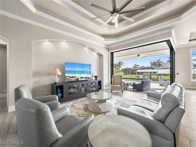 living room featuring ornamental molding, a tray ceiling, ceiling fan, and baseboards