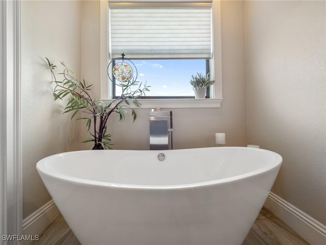 bathroom featuring wood finished floors, a freestanding tub, and baseboards