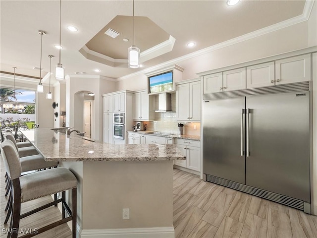 kitchen with a sink, visible vents, appliances with stainless steel finishes, wall chimney range hood, and decorative backsplash