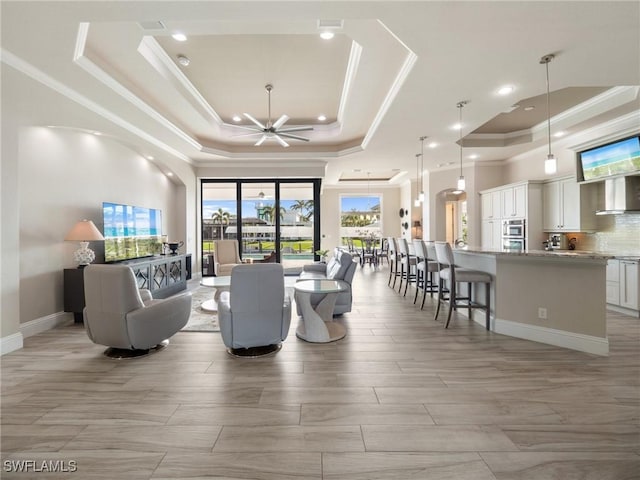 living area featuring ceiling fan, a tray ceiling, and ornamental molding