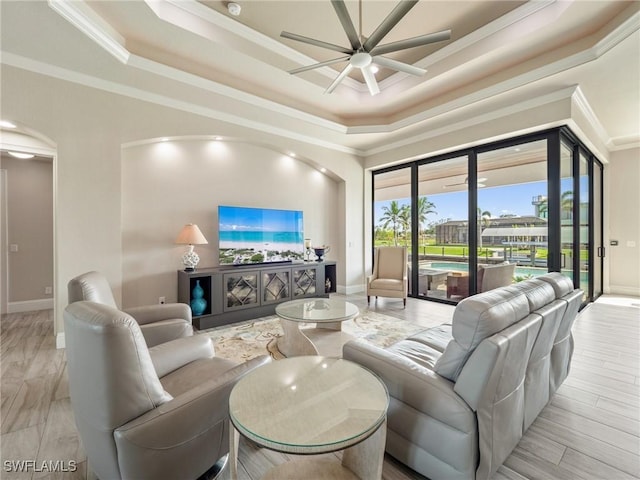 living room featuring a tray ceiling, crown molding, ceiling fan, wood finished floors, and baseboards