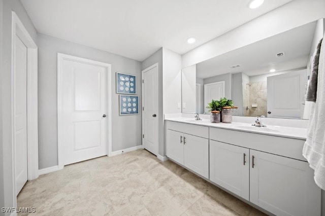 full bath featuring double vanity, tiled shower, a sink, and baseboards