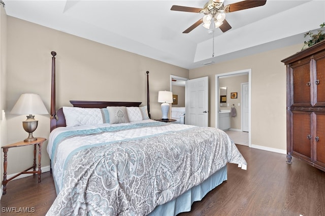 bedroom with dark wood-style floors, a tray ceiling, ensuite bath, and baseboards