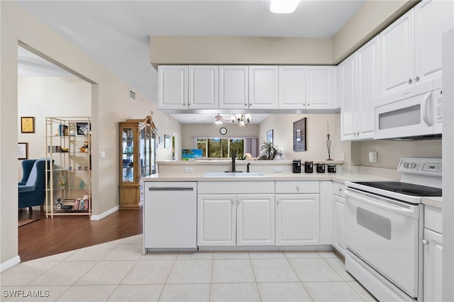 kitchen featuring a peninsula, white appliances, a sink, white cabinetry, and light countertops