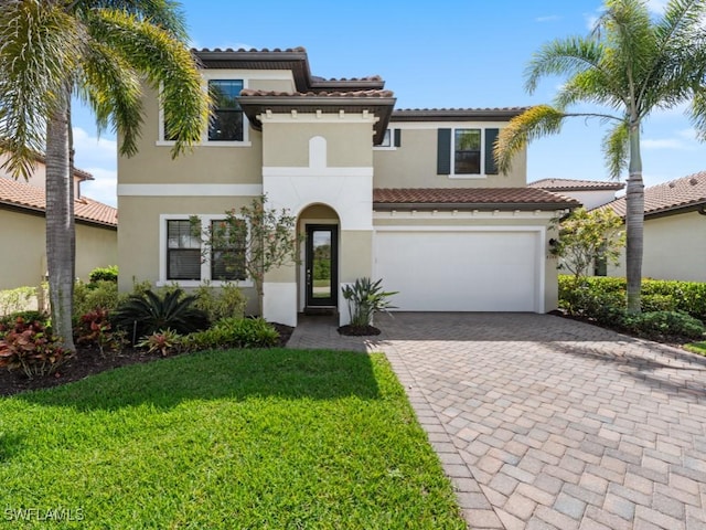 mediterranean / spanish house with decorative driveway, stucco siding, a garage, a tiled roof, and a front lawn