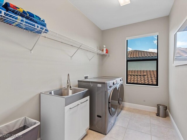 washroom with cabinet space, baseboards, washer and dryer, a sink, and light tile patterned flooring