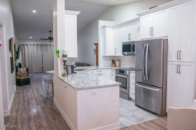 kitchen with appliances with stainless steel finishes, white cabinets, a sink, ceiling fan, and a peninsula