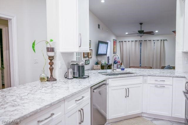 kitchen featuring white cabinets, dishwasher, light stone counters, a peninsula, and a sink