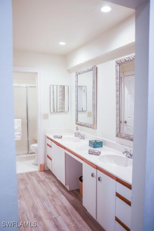 bathroom featuring double vanity, toilet, a stall shower, a sink, and wood finished floors