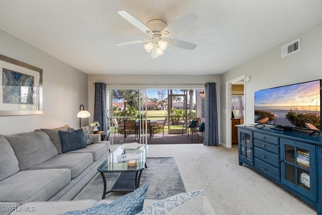 living area featuring a textured ceiling, a ceiling fan, visible vents, and light colored carpet