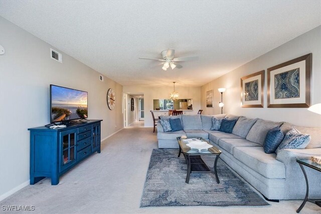 living room featuring ceiling fan with notable chandelier, visible vents, baseboards, and light colored carpet