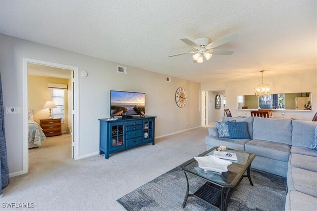 living room with light carpet, baseboards, visible vents, a textured ceiling, and ceiling fan with notable chandelier