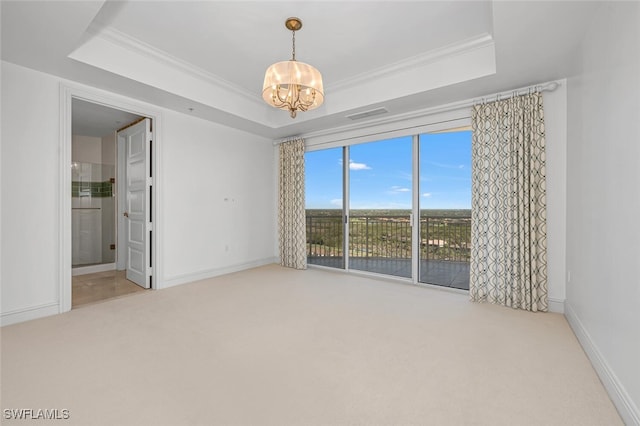 carpeted spare room with a tray ceiling, a notable chandelier, and ornamental molding