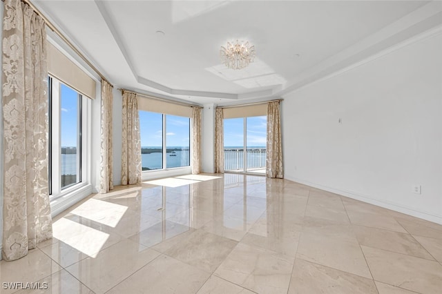 empty room with a tray ceiling, a water view, baseboards, and an inviting chandelier