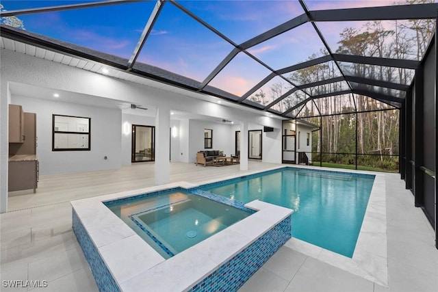 pool at dusk featuring glass enclosure, a pool with connected hot tub, outdoor lounge area, and a patio