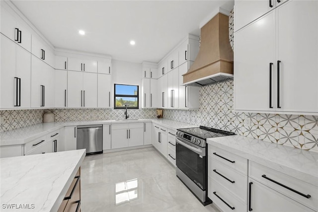 kitchen with light stone counters, a sink, white cabinets, appliances with stainless steel finishes, and custom range hood