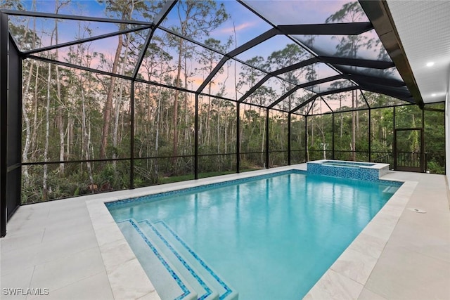 pool at dusk featuring a pool with connected hot tub, glass enclosure, and a patio