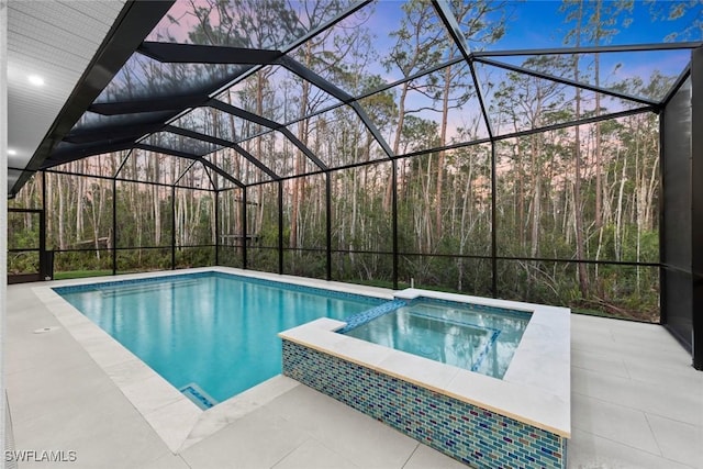 pool at dusk with glass enclosure, a patio, and a pool with connected hot tub