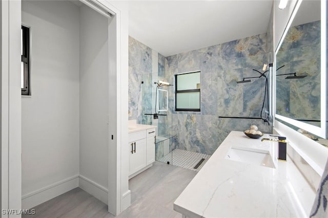 full bath with a marble finish shower, baseboards, tile walls, and vanity