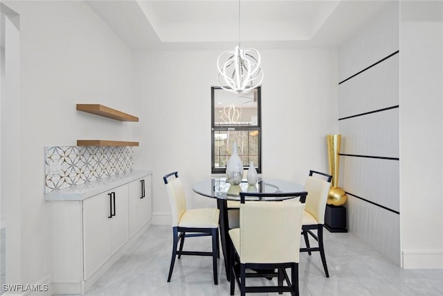 dining room with marble finish floor, a raised ceiling, and a notable chandelier