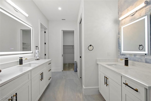 bathroom with a spacious closet, two vanities, and a sink