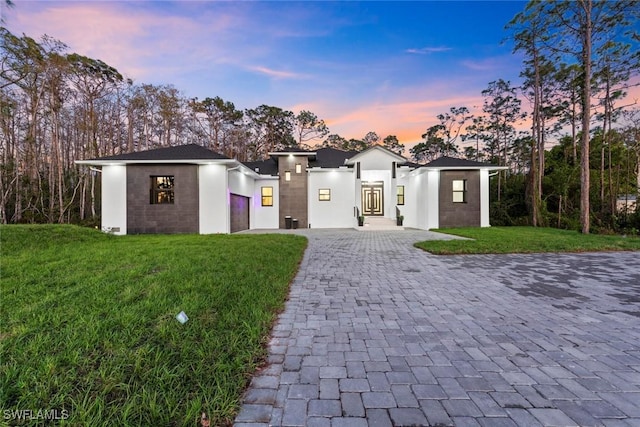 view of front of house with a garage, stucco siding, decorative driveway, and a yard