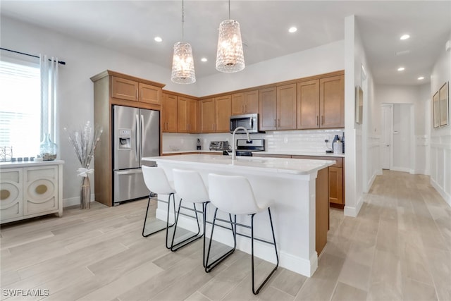 kitchen featuring a breakfast bar, light countertops, backsplash, appliances with stainless steel finishes, and an island with sink