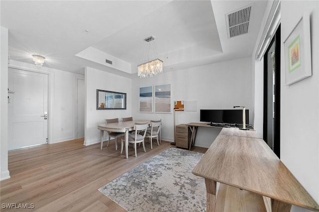 interior space featuring a tray ceiling, visible vents, baseboards, and wood finished floors