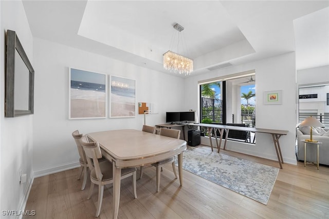 dining space with light wood finished floors, a raised ceiling, visible vents, and baseboards