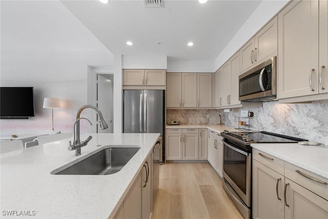 kitchen with light stone counters, tasteful backsplash, appliances with stainless steel finishes, a sink, and light wood-type flooring